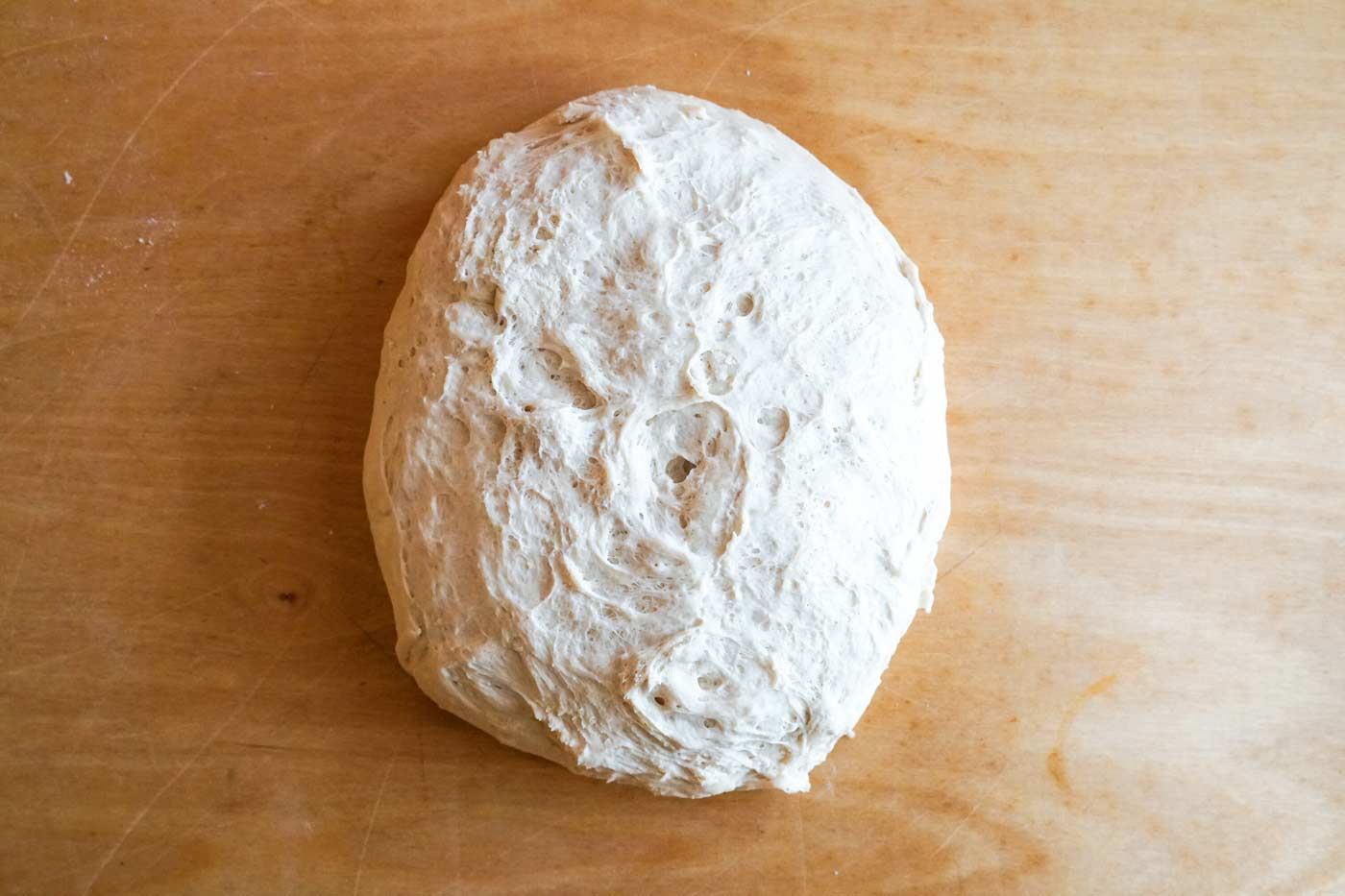 A round of bread dough resting on a wooden board