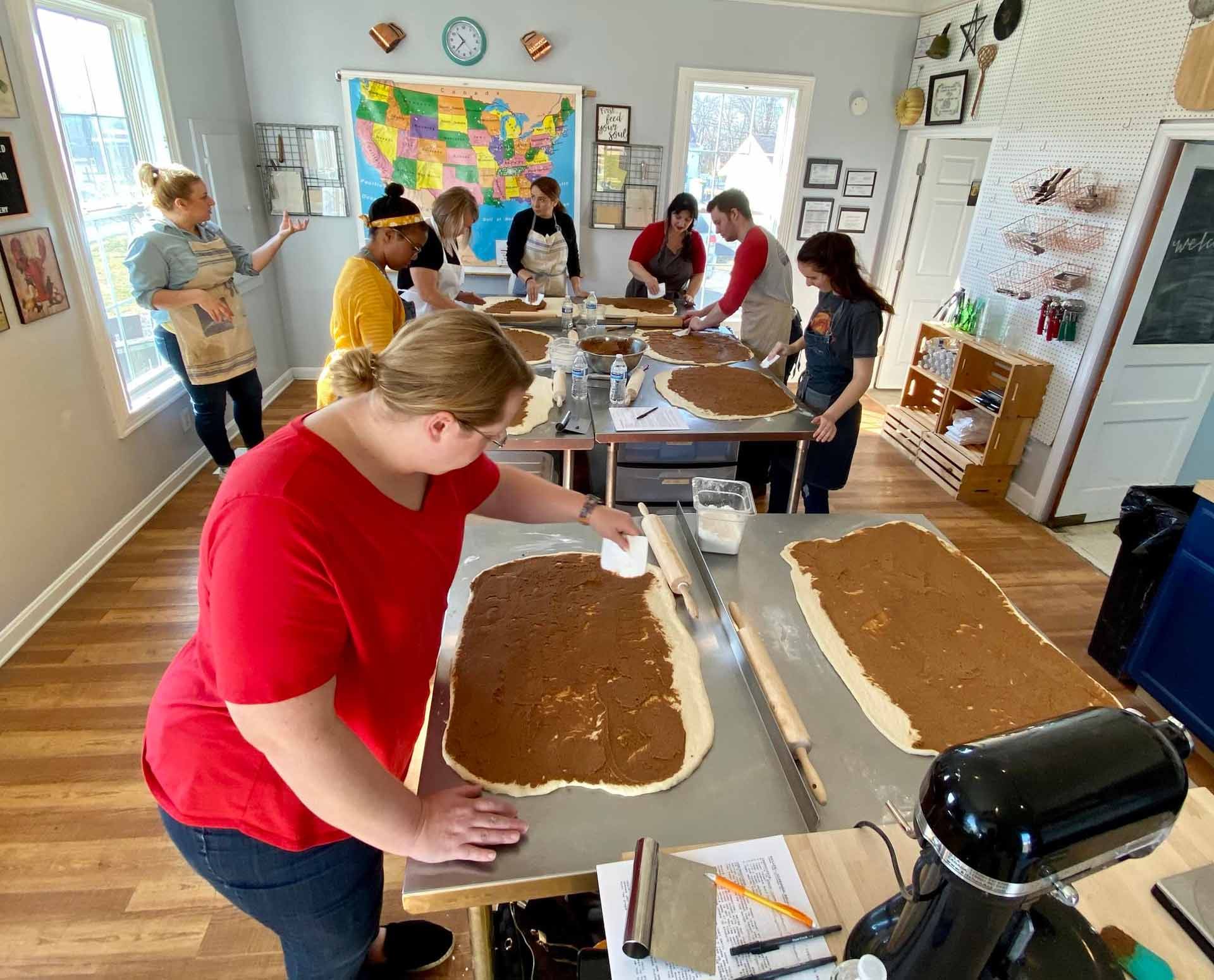 Sarah Gonzalez rolling out cinnamon roll dough with students at a baking class