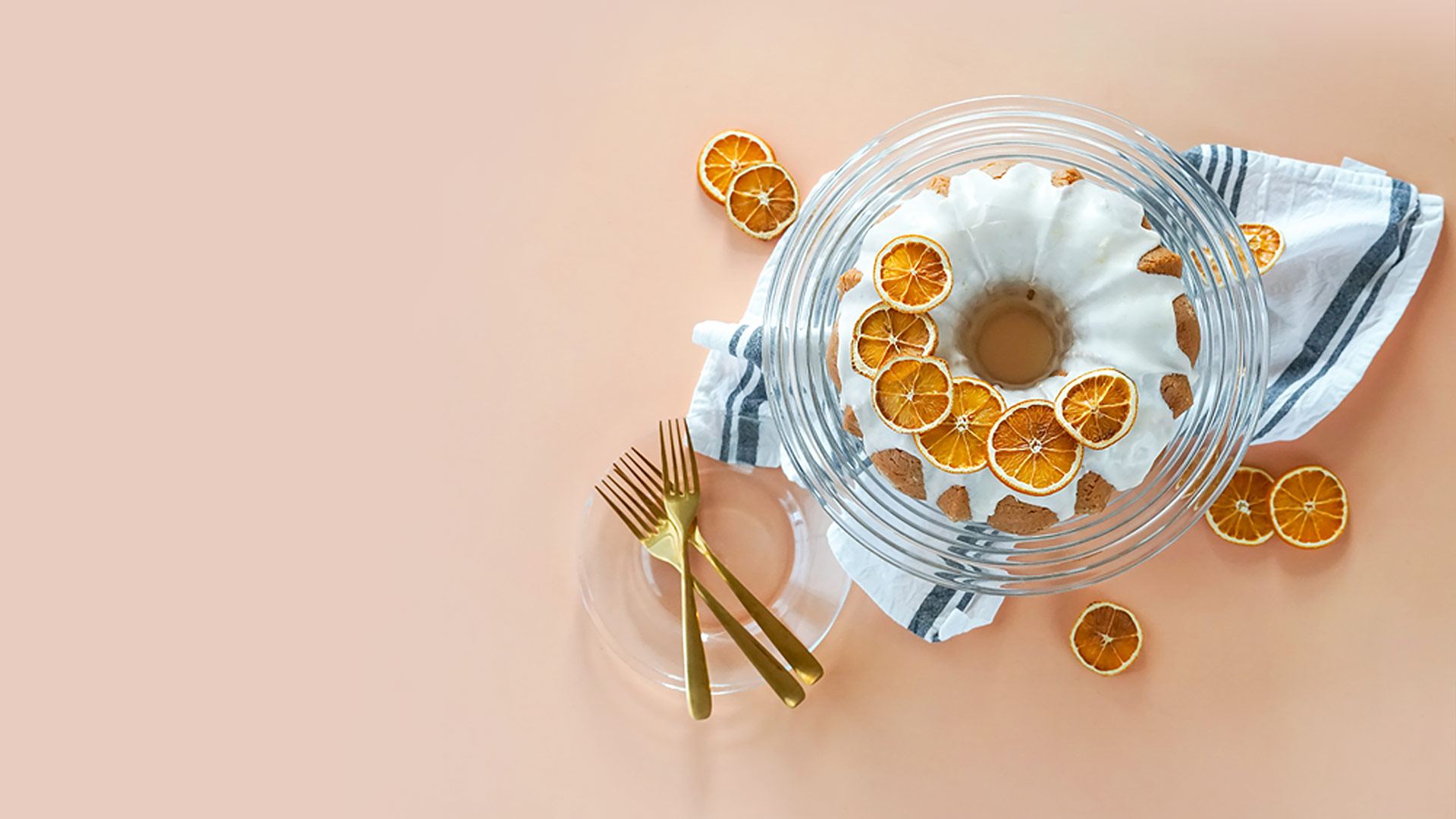 A glazed bundt cake with candied orange on a peach table